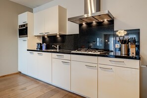 A modern kitchen with white cabinets, a black countertop, and stainless steel appliances. - Modern Apartment in Den Haag (Den Haag)