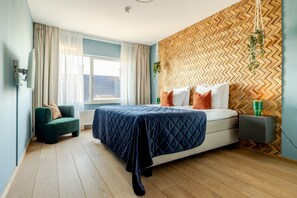A modern bedroom with a bed, a chair, a bedside table, and a herringbone-patterned wall. - Modern Apartment in Den Haag (Den Haag)