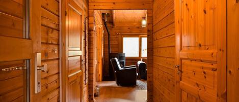 A wooden cabin interior with a narrow hallway leading to a seating area with a fireplace.