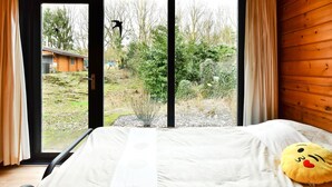Een kamer met een bed, een raam met gordijnen en uitzicht op een tuin en een gebouw.
