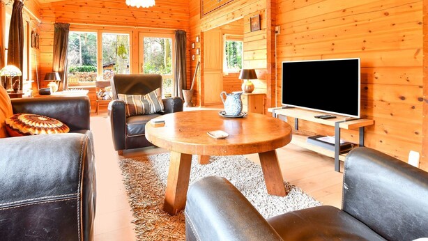 Een knus houten interieur met een ronde houten tafel, leren banken, een televisie en een open haard.