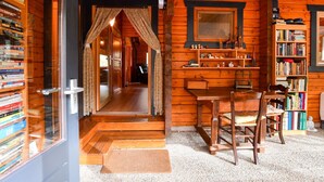 Een knus houten blokhut interieur met een houten trap, een eethoek met een tafel en stoelen, en een boekenplank vol boeken.