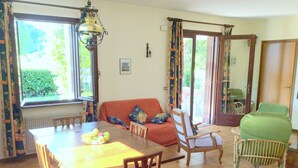 A dining area with a wooden table, chairs, and a red sofa. There is a window with curtains, a door, and a mirror on the wall. - Villa in Northern Italy near Borgo di Toppo (Travesio)