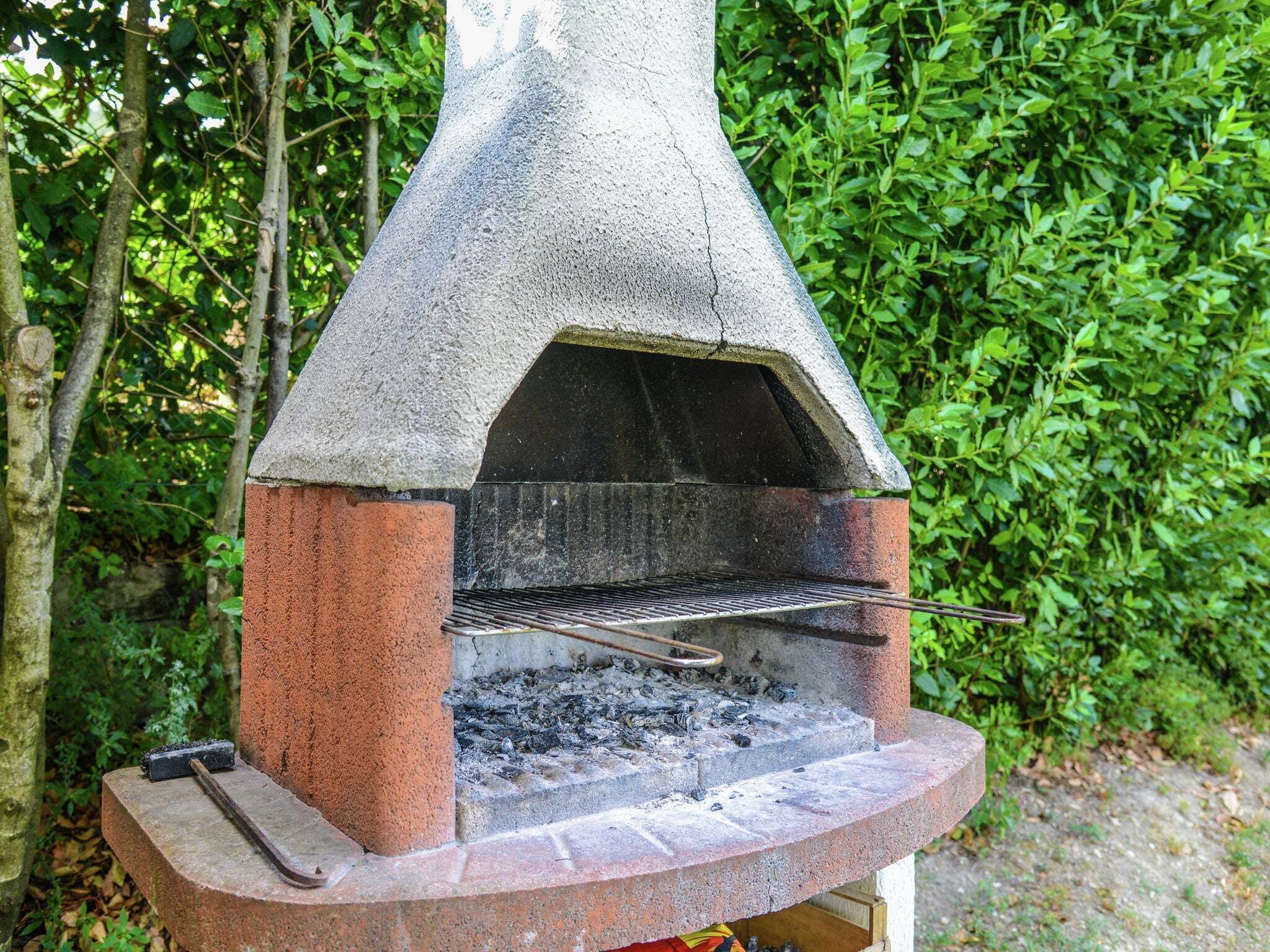 A stone-built outdoor grill with a chimney, surrounded by greenery.