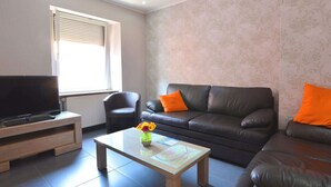 A modern living room with a leather sofa, a flat-screen TV, and a coffee table with a vase of flowers.