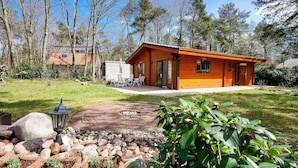 Une cabane en bois dotée d’un patio, entourée d’arbres et d’un jardin bien entretenu.
