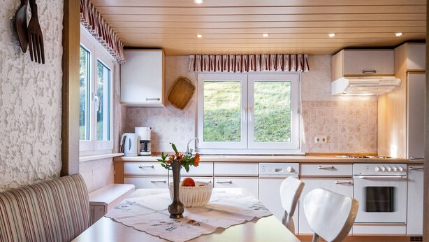 Uma cozinha compacta com área de jantar, incluindo uma mesa com cadeiras, cafeteira e janela com vista para o verde.