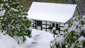 Um edifício coberto de neve com estilo arquitetônico tradicional, rodeado por árvores carregadas de neve e um caminho estreito.