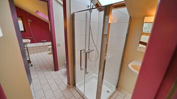 A modern bathroom with a glass shower enclosure, a white sink, and a red accent wall.