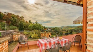 Una terraza con una mesa lista para cuatro personas, rodeada de muros de ladrillo y una vista panorámica de colinas y árboles.