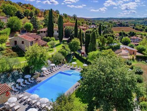 Una gran piscina con tumbonas y sombrillas, rodeada de exuberante vegetación y edificios de piedra.
