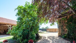 A covered outdoor area with a gravel path, a wooden pergola, and a stone building with a tiled roof. - Tranquil Escape in Loubejac (Loubejac)
