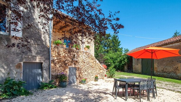 A rustic stone building with a gravel patio, outdoor seating, and a red umbrella. - Tranquil Escape in Loubejac (Loubejac)