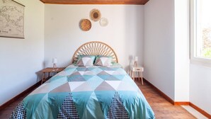 A bedroom with a wooden ceiling, a bed with a geometric-patterned bedspread, a wicker hanging light fixture, and a map on the wall. - Tranquil Escape in Loubejac (Loubejac)