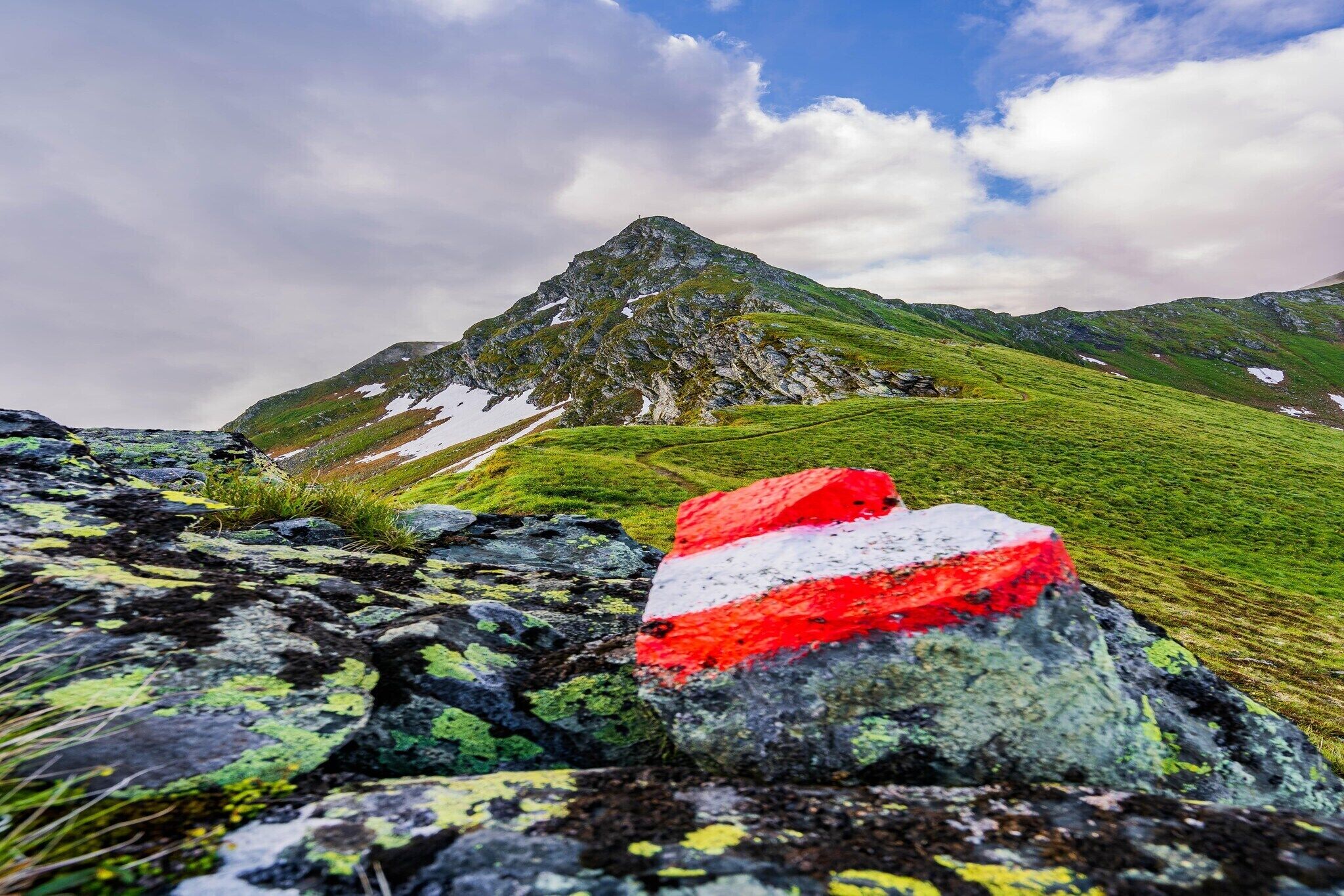 Berglandschaft mit felsigem Vordergrund und einer Flagge auf einem Felsen.