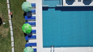 Vista aerea di una piscina con lettini blu e ombrelloni verdi, circondata da un solarium piastrellato.