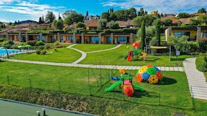 Un cortile alberghiero con un’area giochi, una piscina e un vialetto che conduce all'ingresso.