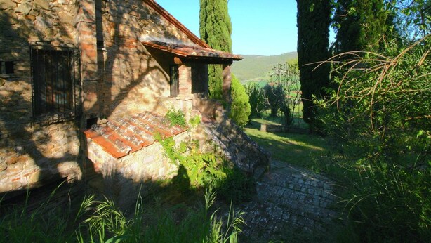 A stone building with a tiled roof, surrounded by greenery and a clear sky.
