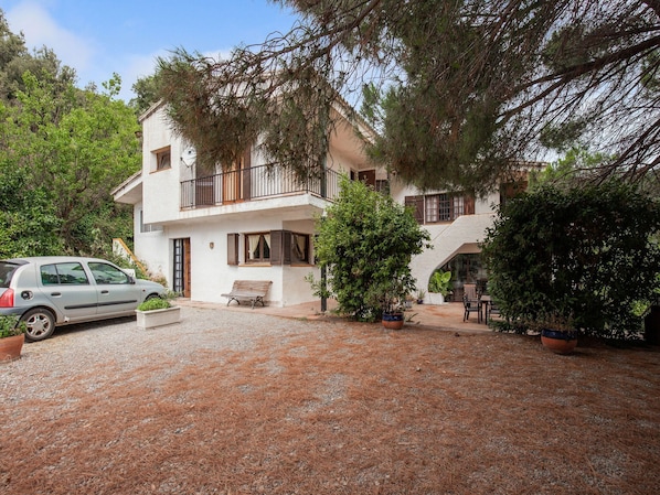 A two-story building with a balcony, a gravel driveway, and a parked car.