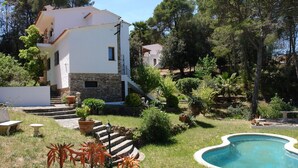 A two-story house with a stone base and white upper walls, surrounded by a well-maintained garden with a swimming pool. - Belvilla by OYO Casa Rey (Begur)