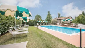 A swimming pool with lounge chairs and umbrellas, surrounded by a well-maintained lawn and stone buildings.