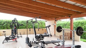 An outdoor gym with various exercise equipment including a treadmill, weight bench, and free weights.