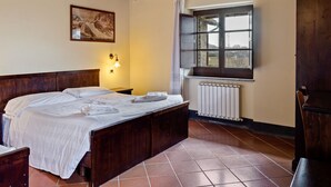 A bedroom with a wooden bed, a nightstand, a window with a view, and a radiator.