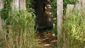 Una construcció de fusta amb una porta, envoltada d'herba alta i una tanca de fusta.