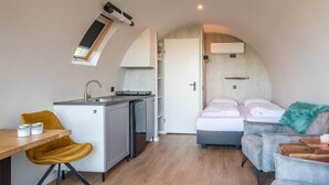 Habitació compacta amb cuina americana, zona de menjador i llit amb una manta verda.
