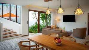 A modern living room with a wooden dining table, wicker chairs, a sofa, and a TV mounted on the wall. - WAKA VILLA Private Resort & Spa 16 + Adults Only (Siem Reap)