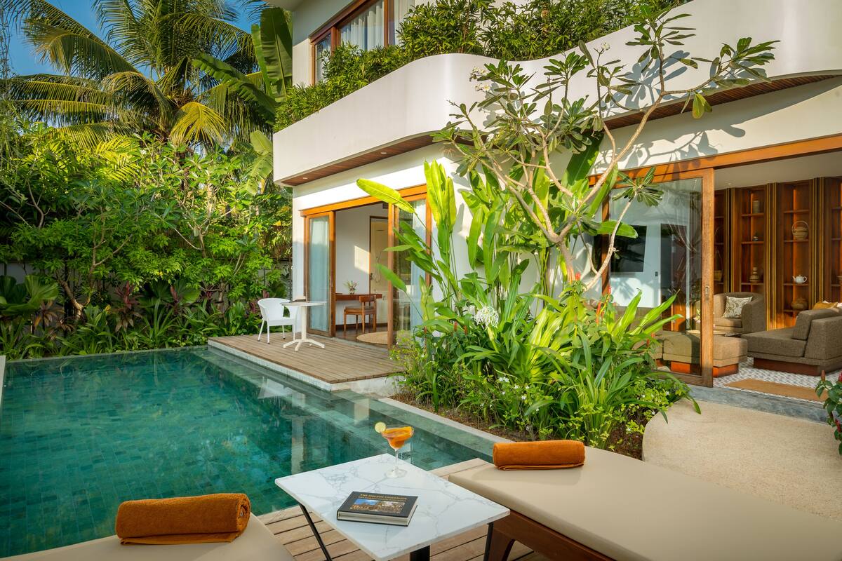 Una casa moderna con piscina, mobiliario exterior y abundante vegetación.
