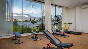 A modern gym with various exercise equipment, large windows, and a view of greenery and water.