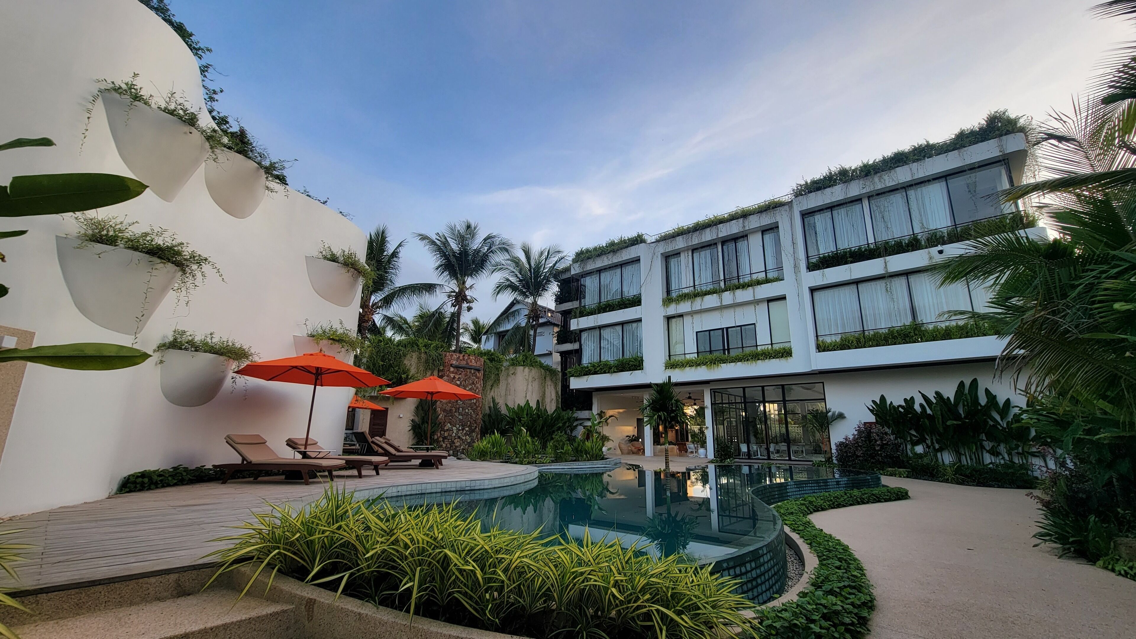 A modern hotel with a pool, sun loungers, and red umbrellas.