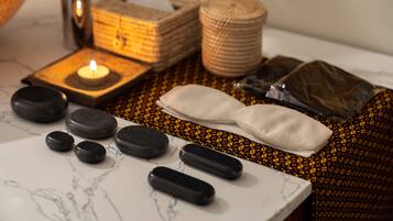 A massage therapy setup with stones, a candle, and a towel on a patterned surface.