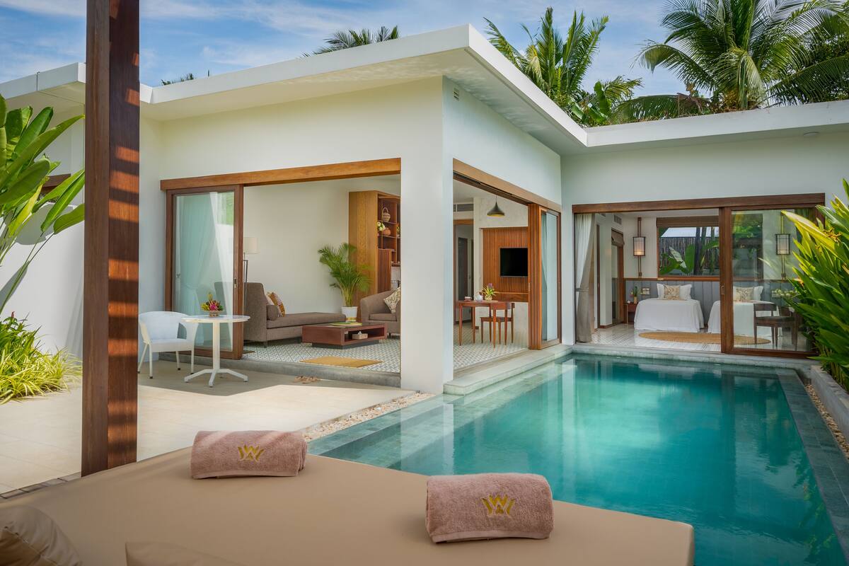 Una habitación de hotel moderna con piscina, zona de estar con sofá y mesa, y un dormitorio con cama y baño.