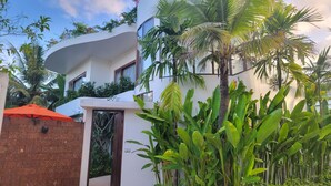 A modern building with a curved facade, surrounded by lush tropical plants and palm trees. - WAKA VILLA Private Resort & Spa 16 + Adults Only (Siem Reap)