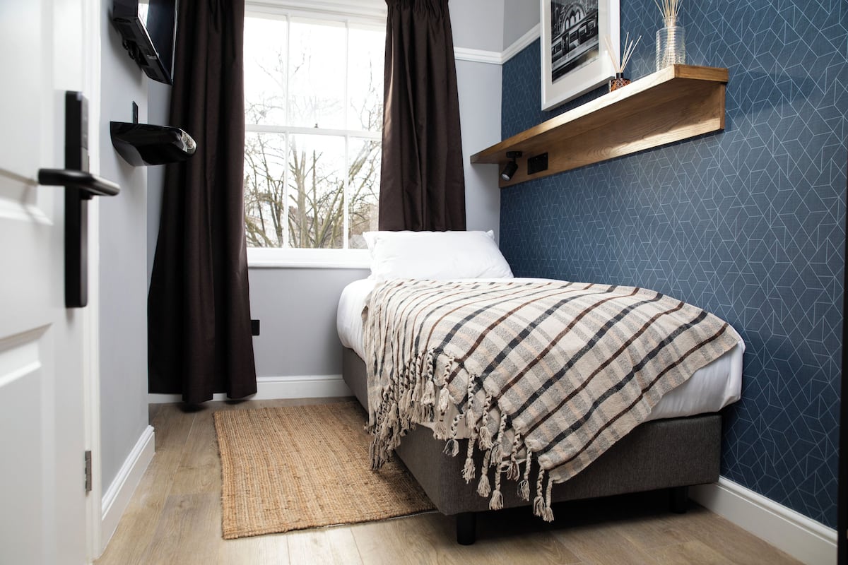 A bedroom with a bed, a window, a door, and a wall-mounted shelf.