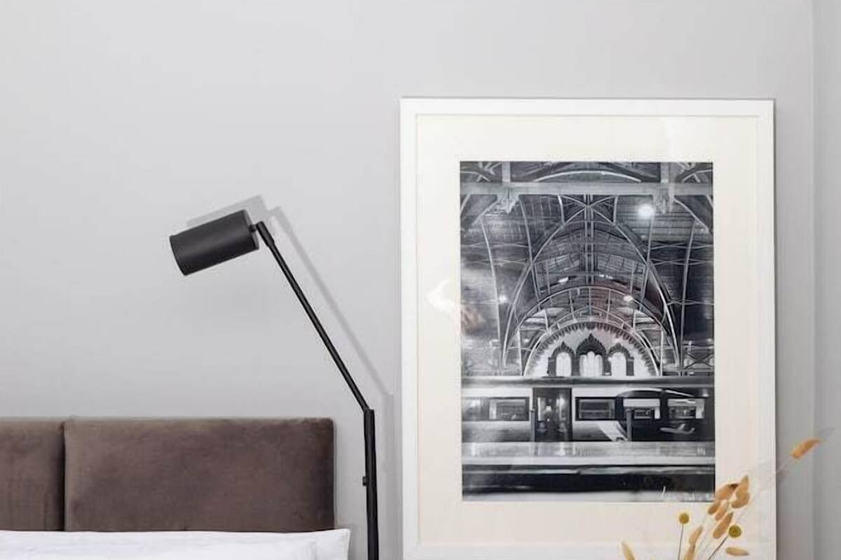 A neatly arranged bedroom with a bed, a bedside table with glasses, and a framed picture on the wall.