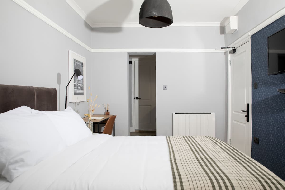 A bedroom with a bed, bedside table, lamp, and a door leading to another room.