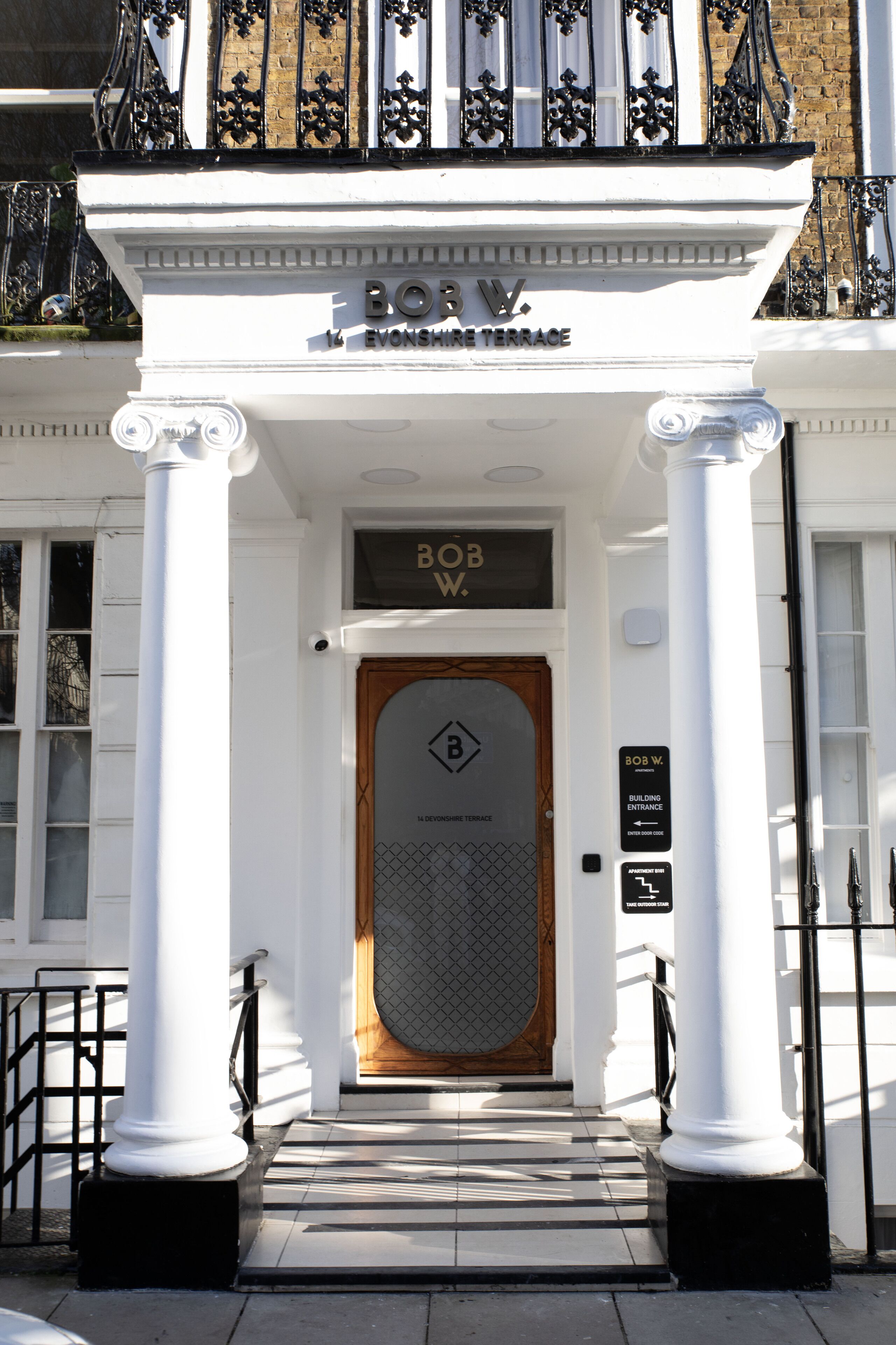 Une entrée d’immeuble avec une enseigne indiquant « BOSW. EVONSHEE TERRACE » et une porte ornée d’un motif géométrique.