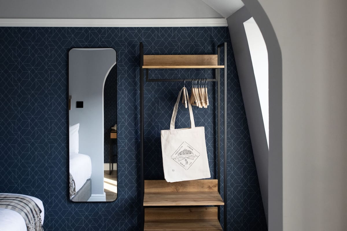 A bedroom with a bunk bed, a mirror, a wooden shelf with bags, and a patterned wall.