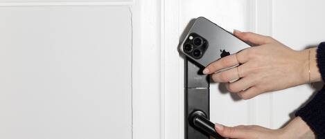 A hand holding a smartphone near a door handle.