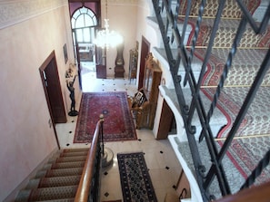 Un magnifique escalier orné de balustrades travaillées, un lustre et des tapis à motifs.