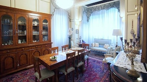 Ein traditioneller Speisesaal mit einem Holzschrank, einem Esstisch und Stühlen. Angrenzend befindet sich ein Wohnbereich mit einer Couch und einer Lampe.