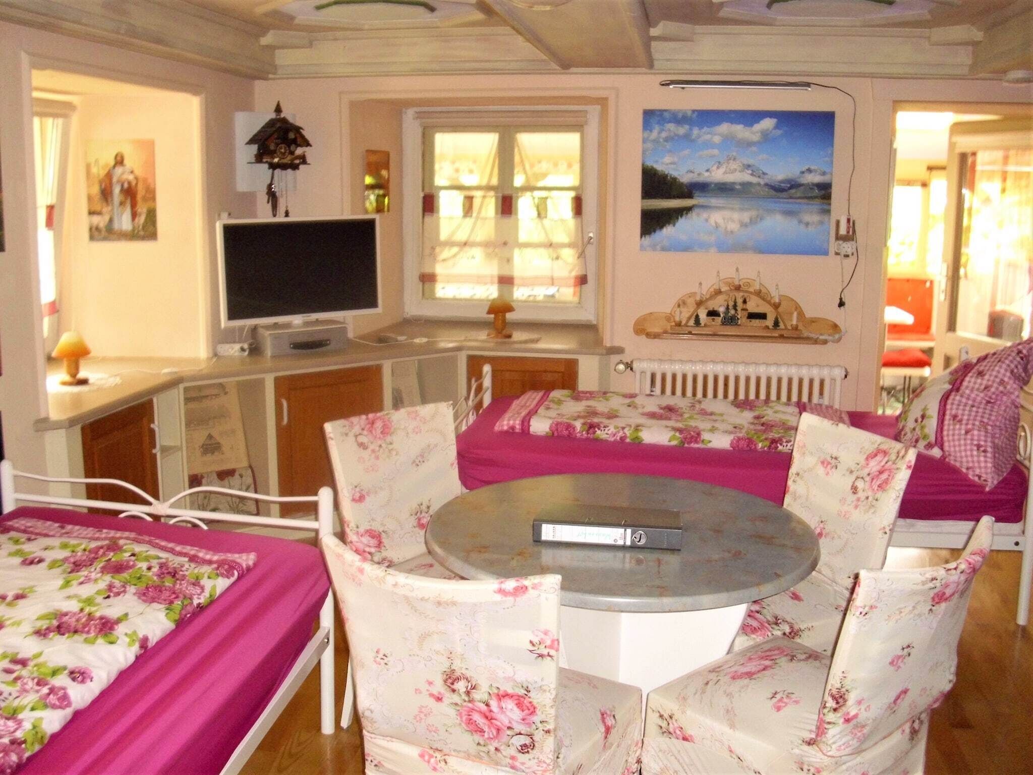 Una habitación acogedora con una cama, una mesa redonda, sillas con estampado floral, un televisor y un cuadro de un lago.