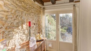 A room with a stone wall, a wooden dresser, a glass cabinet, and a view of greenery outside.