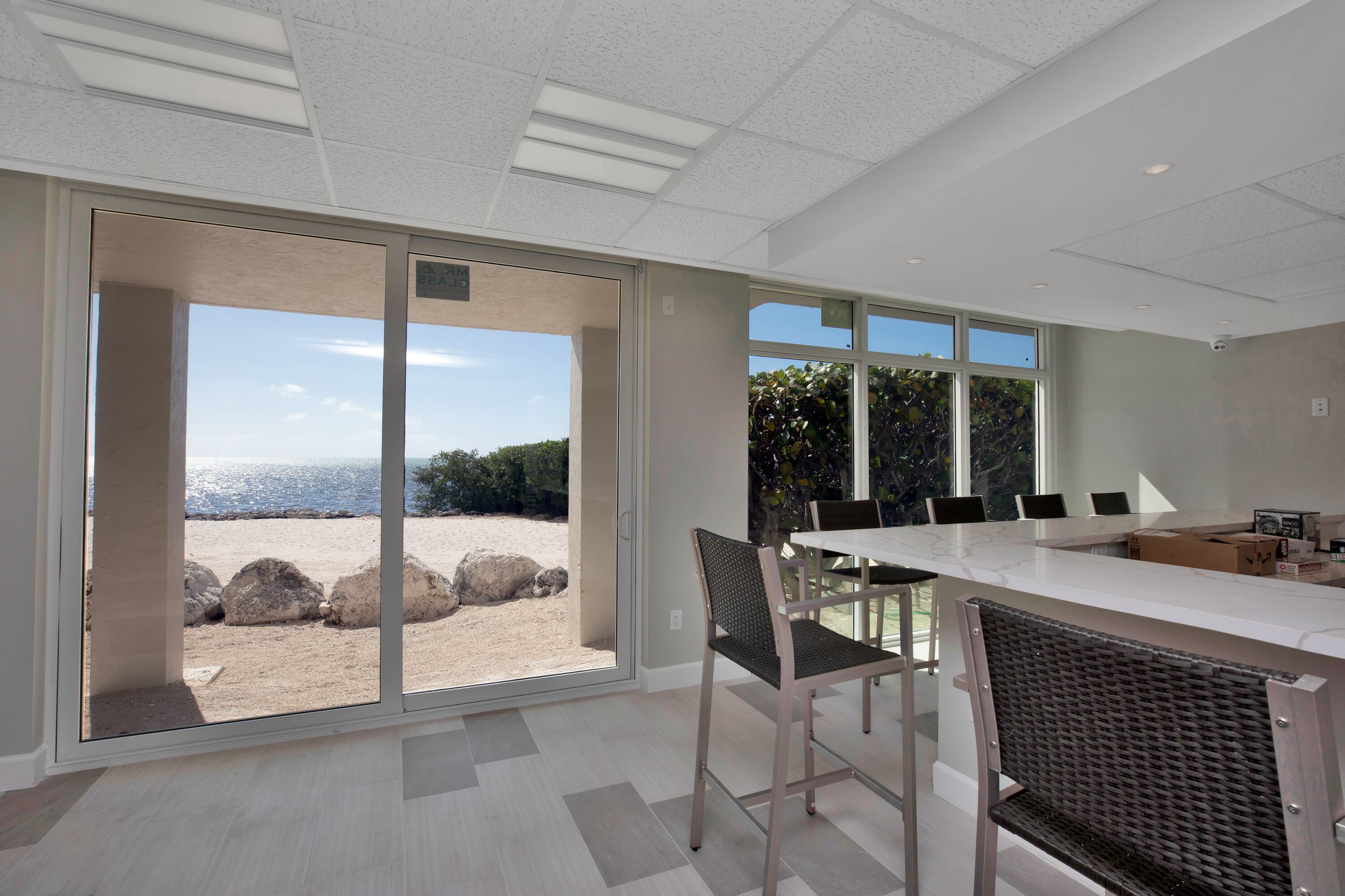 A modern kitchen with a large island, sliding glass doors leading to a beach view, and a dining area with chairs and a table.