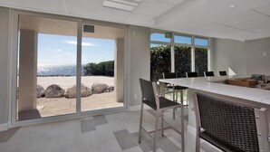 A modern kitchen with a large island, sliding glass doors leading to a beach view, and a dining area with chairs and a table. - Reel Paradise at Sea Gulls (Tavernier)