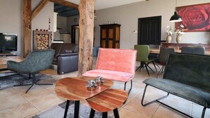 A spacious living area with a wooden ceiling, a television, a fireplace, and a dining table with chairs. - Apartment in Netherlands near Nature Trails (Dalerveen)