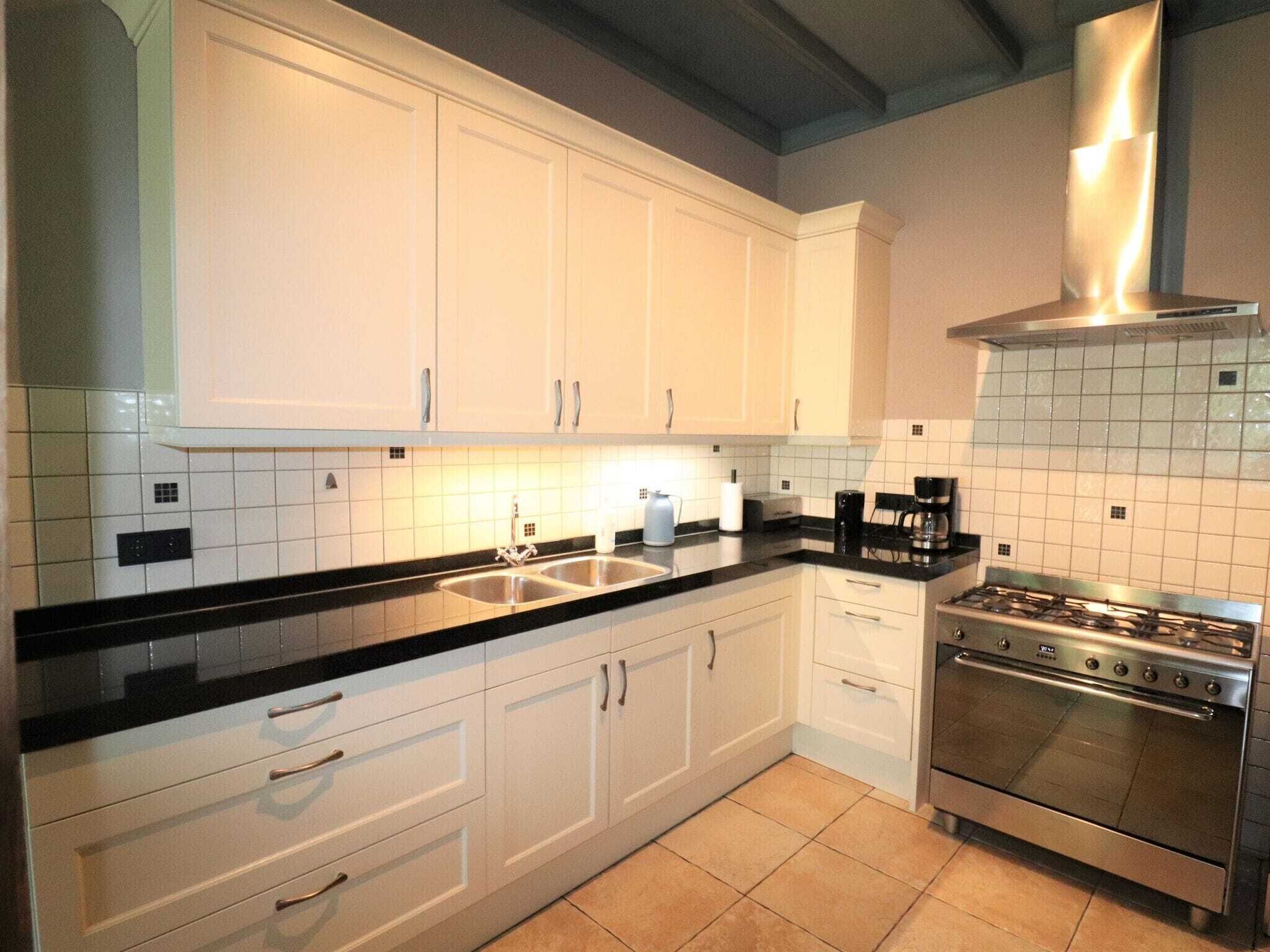 A kitchen with white cabinets, a black countertop, a gas stove, and a tiled backsplash.